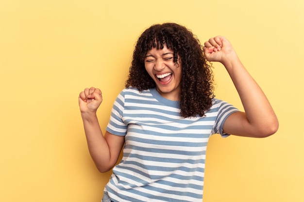 Young mixed race woman isolated on yellow background dancing and having fun