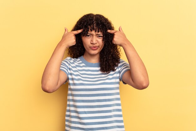 Young mixed race woman isolated on yellow background focused on a task, keeping forefingers pointing head.