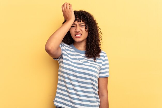 Young mixed race woman isolated on yellow background forgetting something, slapping forehead with palm and closing eyes.