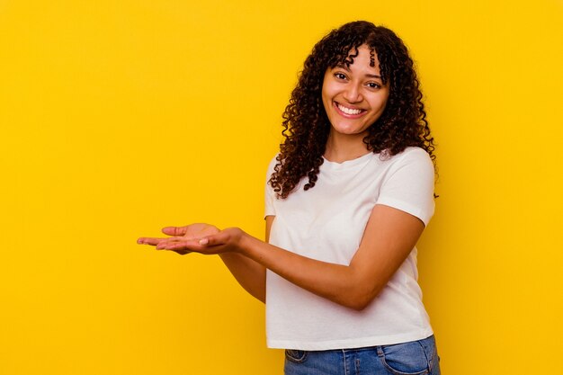 Young mixed race woman isolated on yellow background holding a copy space on a palm.