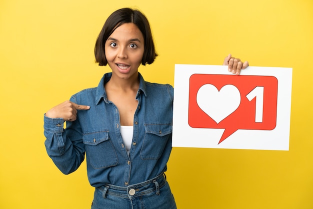 Young mixed race woman isolated on yellow background holding a placard with Like icon and pointing it