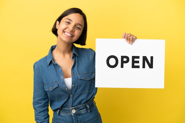 Young mixed race woman isolated on yellow background holding a placard with text OPEN with happy expression