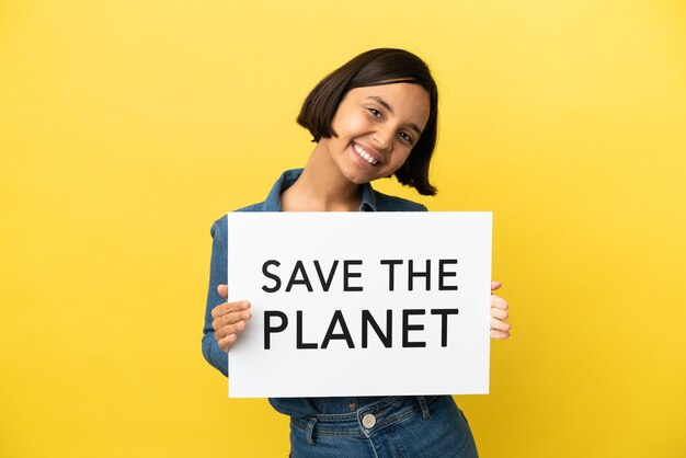 young mixed race woman isolated on yellow background holding a placard with text save the planet with happy expression