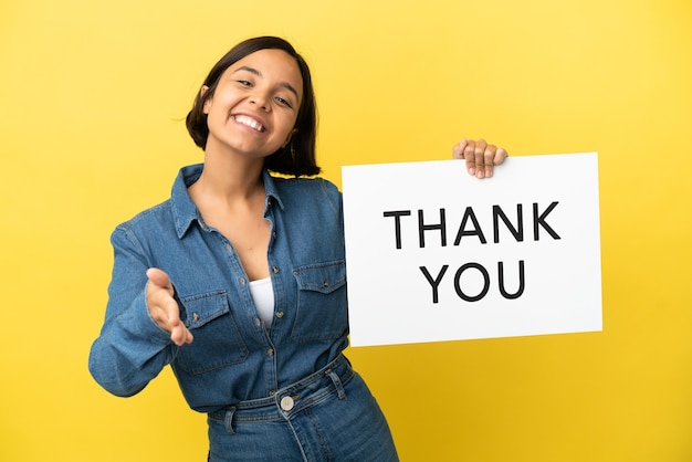 Young mixed race woman isolated on yellow background holding a placard with text THANK YOU making a deal