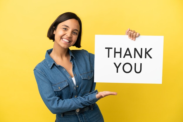Photo young mixed race woman isolated on yellow background holding a placard with text thank you and  pointing it
