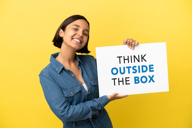 Young mixed race woman isolated on yellow background holding a placard with text Think Outside The Box with happy expression