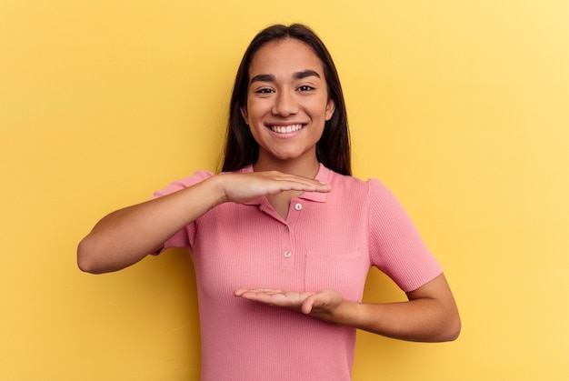 Young mixed race woman isolated on yellow background holding something with both hands, product presentation.