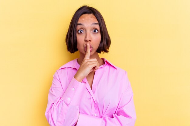 Young mixed race woman isolated on yellow background keeping a secret or asking for silence.