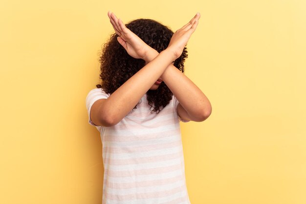 Young mixed race woman isolated on yellow background keeping\
two arms crossed denial concept