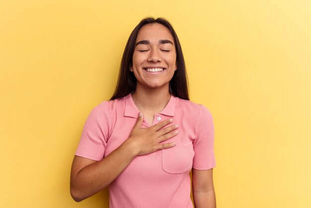 Young mixed race woman isolated on yellow background laughs out loudly keeping hand on chest.