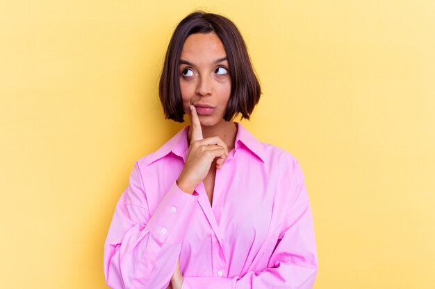 Young mixed race woman isolated on yellow background looking sideways with doubtful and skeptical expression.