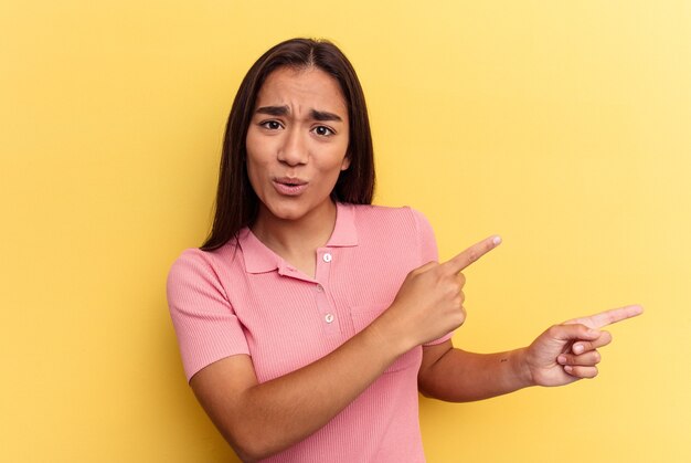 Young mixed race woman isolated on yellow background pointing with forefingers to a copy space, expressing excitement and desire.