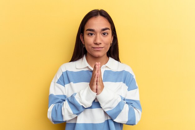 Young mixed race woman isolated on yellow background praying, showing devotion, religious person looking for divine inspiration.