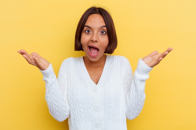 Young mixed race woman isolated on yellow background receiving a pleasant surprise, excited and raising hands.