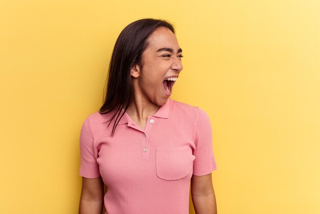 Young mixed race woman isolated on yellow background shouting very angry, rage concept, frustrated.