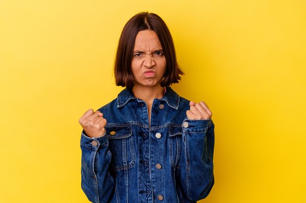 Young mixed race woman isolated on yellow background showing fist to camera, aggressive facial expression.