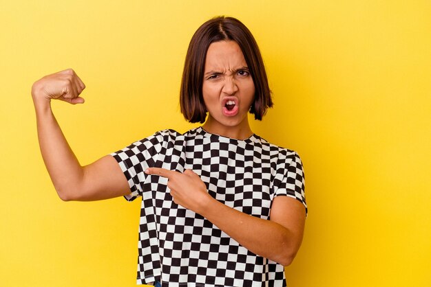 Young mixed race woman isolated on yellow background showing strength gesture with arms, symbol of feminine power