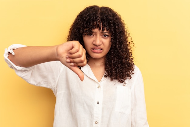 Young mixed race woman isolated on yellow background showing thumb down and expressing dislike.