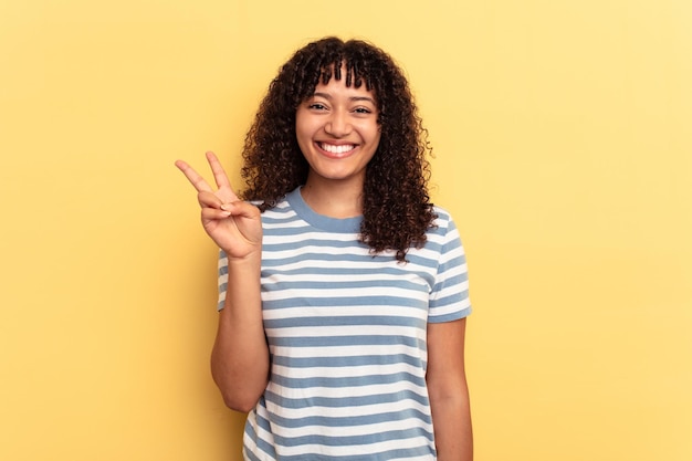 Young mixed race woman isolated on yellow background showing victory sign and smiling broadly