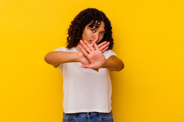 Young mixed race woman isolated on yellow background standing with outstretched hand showing stop sign, preventing you.