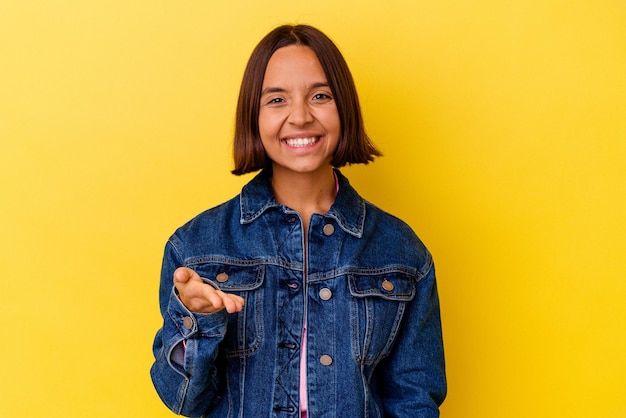 Young mixed race woman isolated on yellow background stretching hand at camera in greeting gesture.