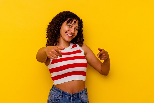 Young mixed race woman isolated on yellow cheerful smiles pointing to front.