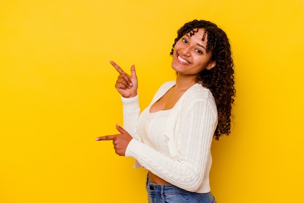 Young mixed race woman isolated on yellow excited pointing with forefingers away.