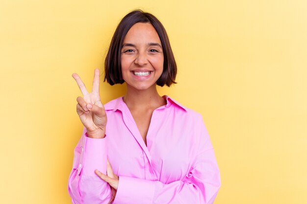 Young mixed race woman isolated on yellow wall joyful and carefree showing a peace symbol with fingers