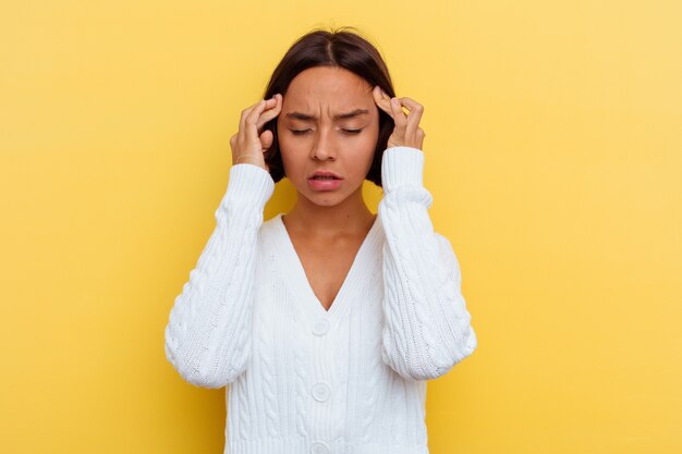 Young mixed race woman isolated on yellow wall touching temples and having headache.