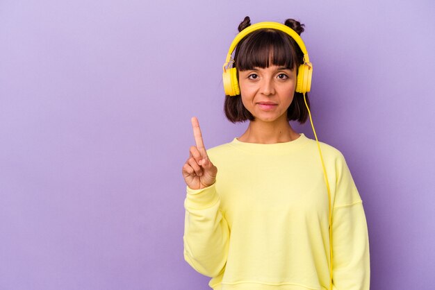 Young mixed race woman listening to music isolated on purple background showing number one with finger