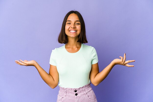 Young mixed race woman makes scale with arms, feels happy and confident.