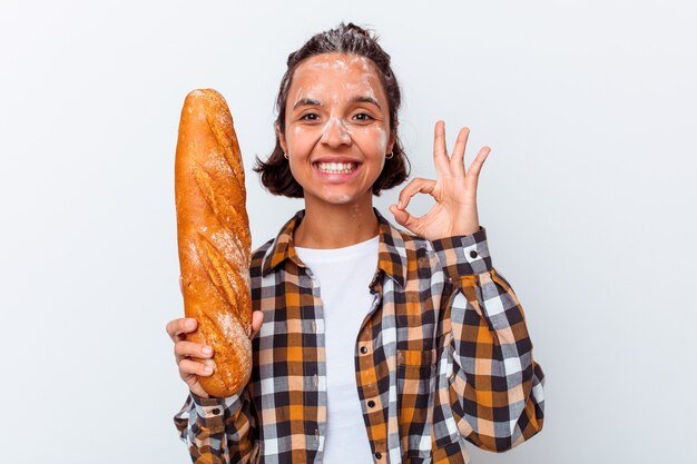 Young mixed race woman making bread isolated on white wall cheerful and confident showing ok gesture.