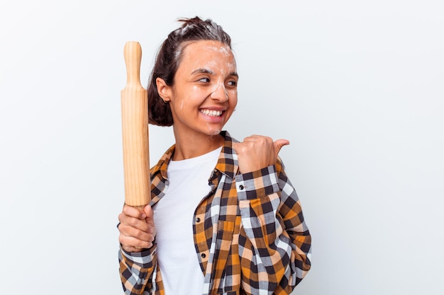 Young mixed race woman making bread isolated on white wall points with thumb finger away, laughing and carefree.