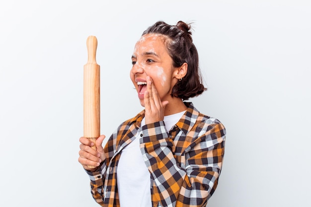 Young mixed race woman making bread isolated on white wall shouting and holding palm near opened mouth.