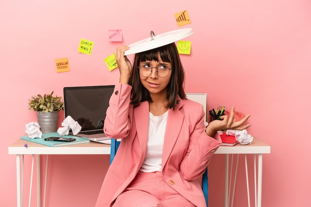 Young mixed race woman preparing a exam in the room holding a paper bin isolated on pink background