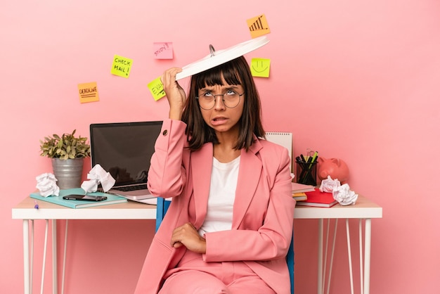 Young mixed race woman preparing a exam in the room holding a paper bin isolated on pink background