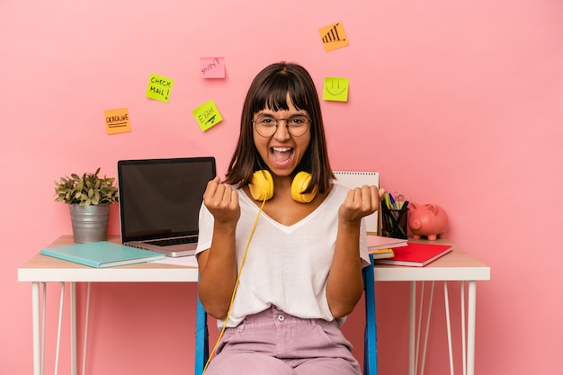 Young mixed race woman preparing a exam in the room listening to music isolated on pink background cheering carefree and excited. Victory concept.