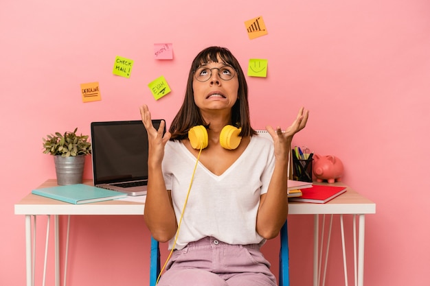 Young mixed race woman preparing a exam in the room listening to music isolated on pink background screaming to the sky, looking up, frustrated.