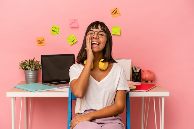 Foto giovane donna di razza mista che prepara un esame nella stanza ascoltando musica isolata su sfondo rosa che grida eccitata davanti.