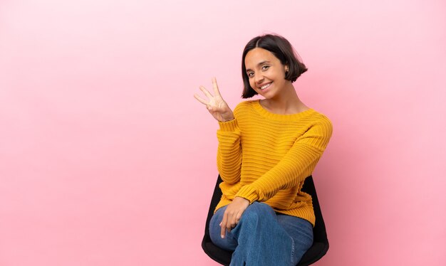 Young mixed race woman sitting on a chair isolated on pink background counting five with fingers