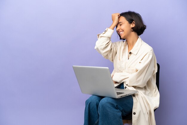 Young mixed race woman sitting on a chair with laptop isolated on purple background has realized something and intending the solution