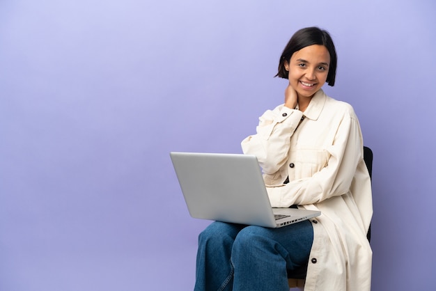 Young mixed race woman sitting on a chair with laptop isolated on purple background laughing