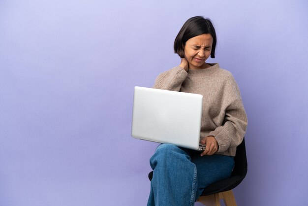 Young mixed race woman sitting on a chair with laptop isolated on purple background with neckache