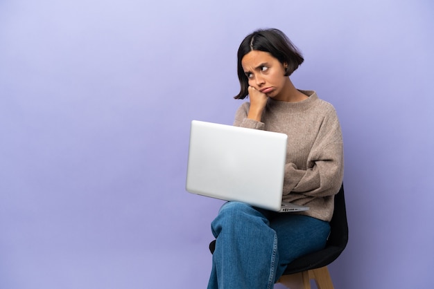 Young mixed race woman sitting on a chair with laptop isolated on purple background with tired and bored expression