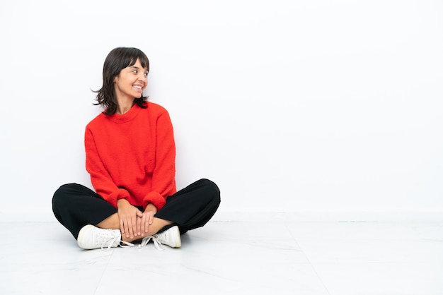 Young mixed race woman sitting on the floor isolated on white background happy and smiling