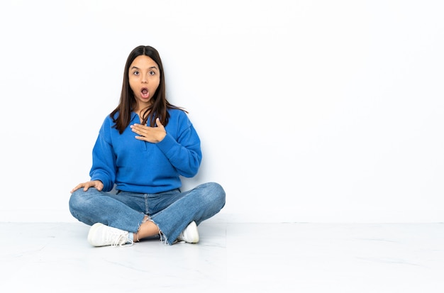 Young mixed race woman sitting on the floor isolated on white surprised and shocked while looking right