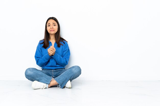 Young mixed race woman sitting on the floor isolated on white wall laughing