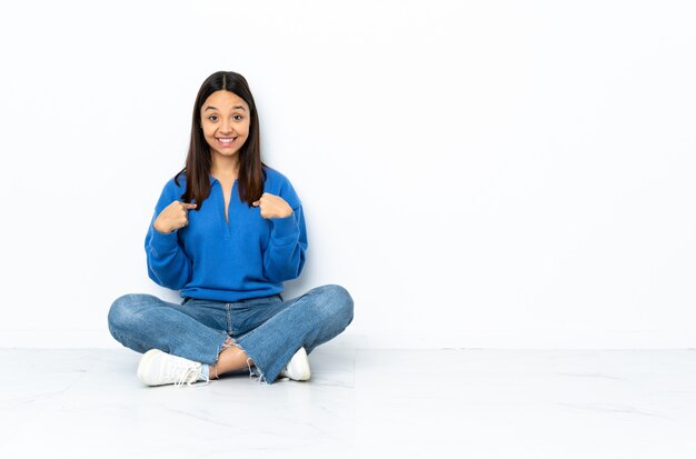 Young mixed race woman sitting on the floor on white wall with surprised facial expression