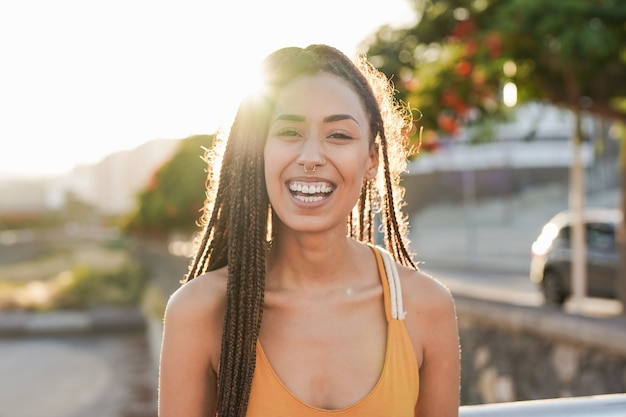 Young mixed race woman smiling on camera in the city with sunset in background