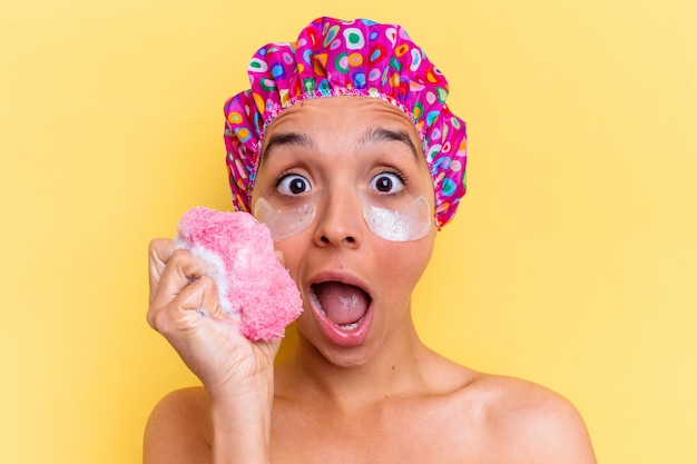 Young mixed race woman taking a bath holding a sponge with an under eye patches